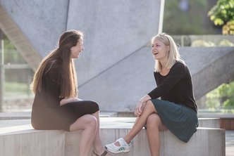 Two students sitting outside university sculpture and talking Photo: Jesper Rais for Aarhus University 